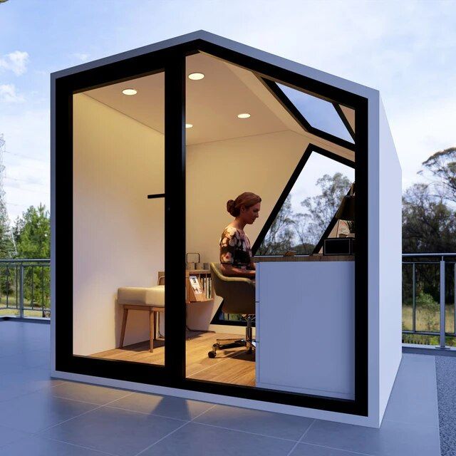 a woman sitting at a desk inside of a small room with glass walls on the outside