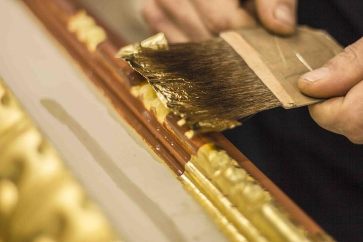 a close up of a person using a brush to paint gold foil on a piece of wood