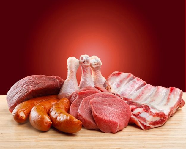 various meats and sausages on a wooden table against a red background with space for text