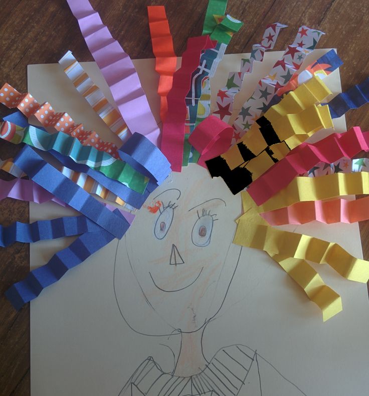 a child's drawing of a turkey with colored strips on the paper and crayons attached to it