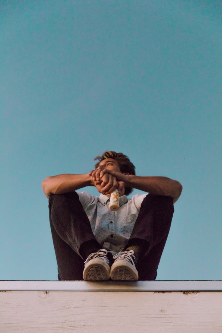 a man sitting on top of a roof holding his hands to his face