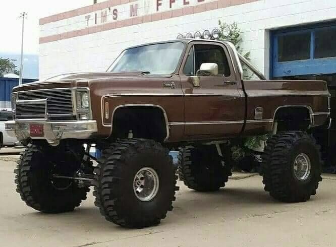 a large brown truck with big tires parked in front of a building on the street