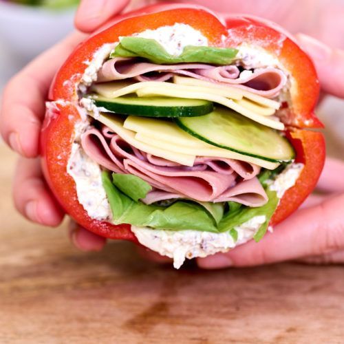 a person holding a sandwich with meat, cheese and vegetables in it on a wooden table