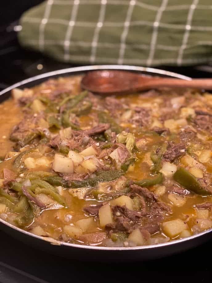 a pot filled with stew sitting on top of a stove next to a wooden spoon