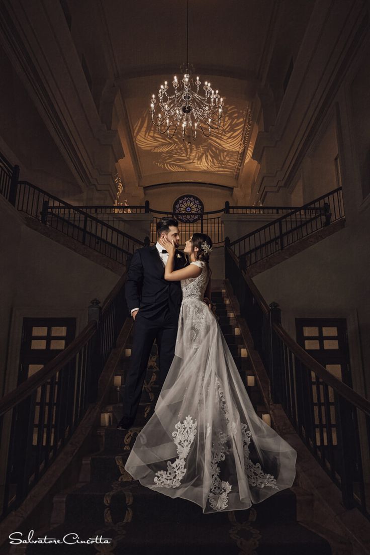 a bride and groom standing on the stairs at their wedding reception in an elegant building