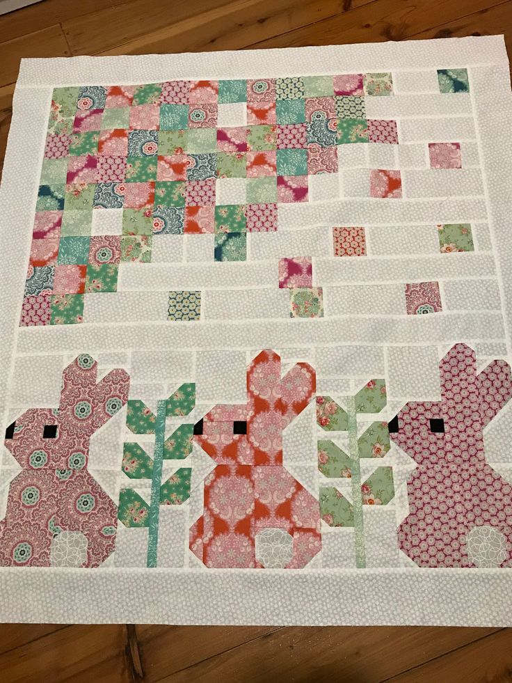 a quilted table topper with two rabbits on it and flowers in the background