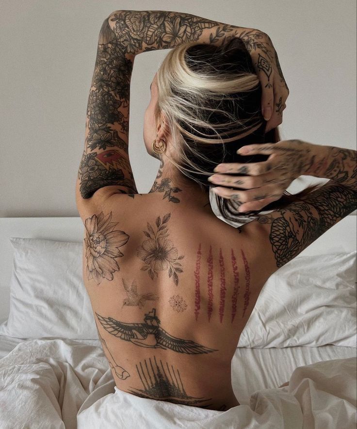 a woman with tattoos on her back sitting in bed