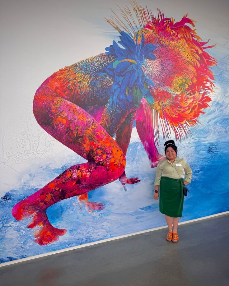 a woman standing in front of a large colorful painting on the side of a building