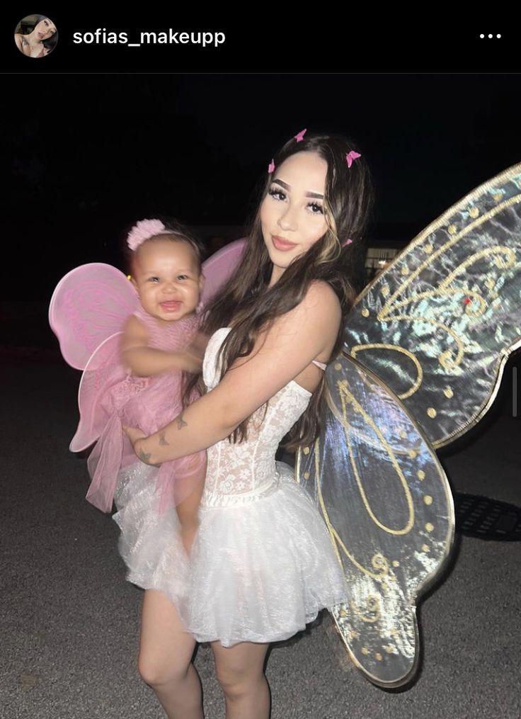 a woman holding a baby in her arms and wearing a fairy costume with wings on it