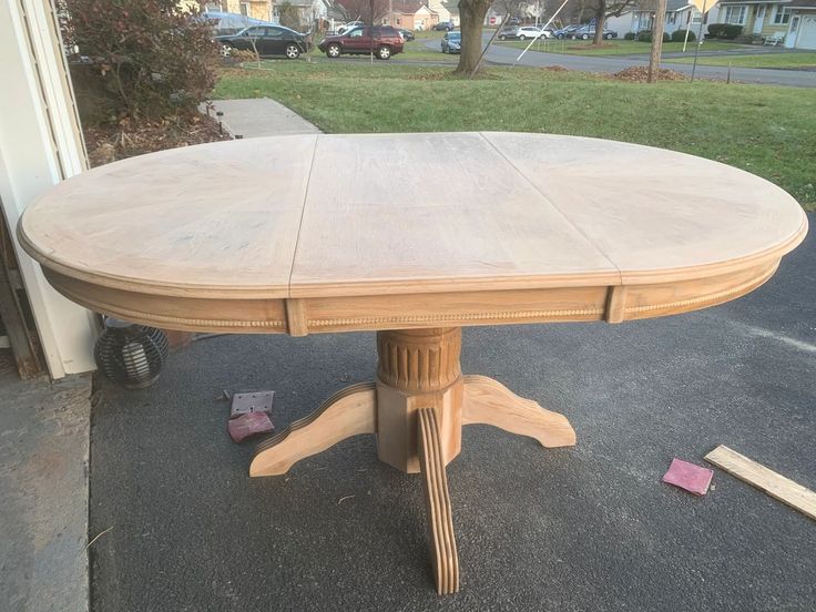 a wooden table sitting in the middle of a driveway next to a house and yard