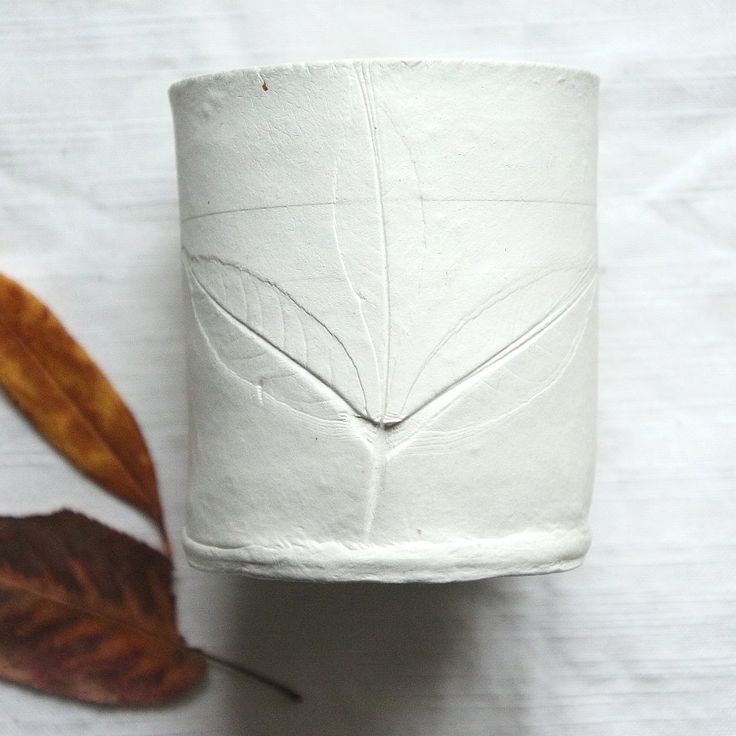 a white vase sitting on top of a table next to a leaf