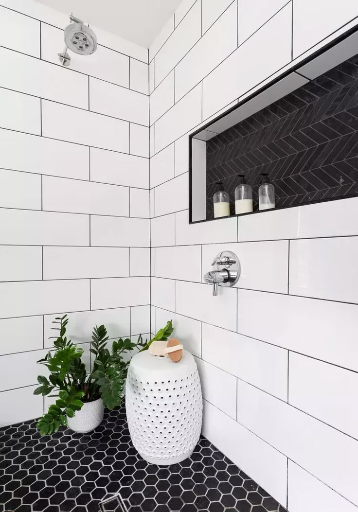 a white bathroom with black and white tile on the walls, potted plants in the corner