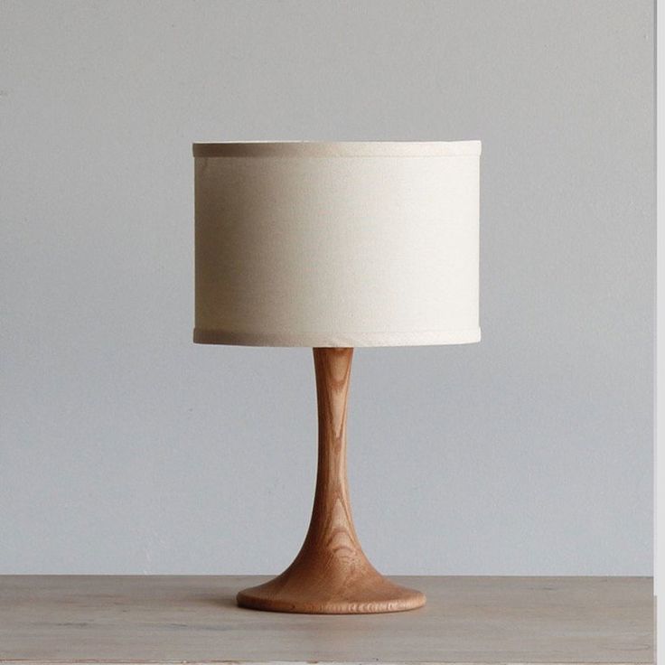 a wooden table lamp with a white shade on it's base, sitting on a shelf