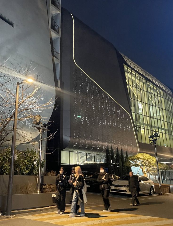 some people are crossing the street in front of a large black building with many windows