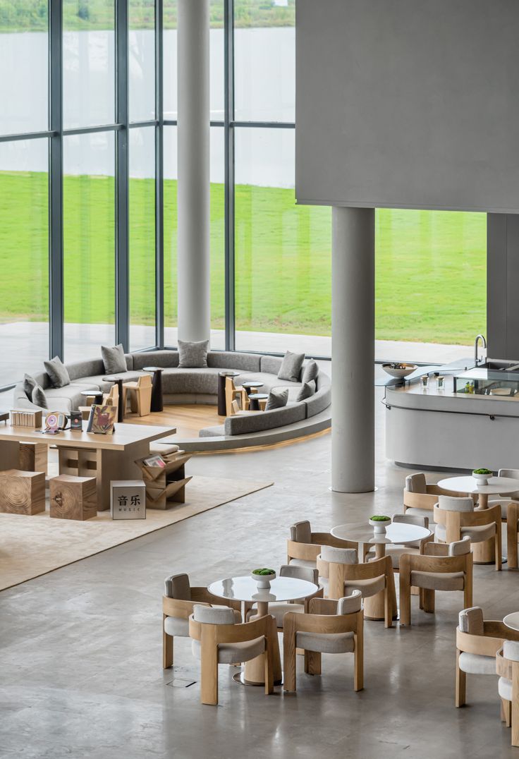 a large open room with tables and couches in front of big windows that look out onto a grassy field