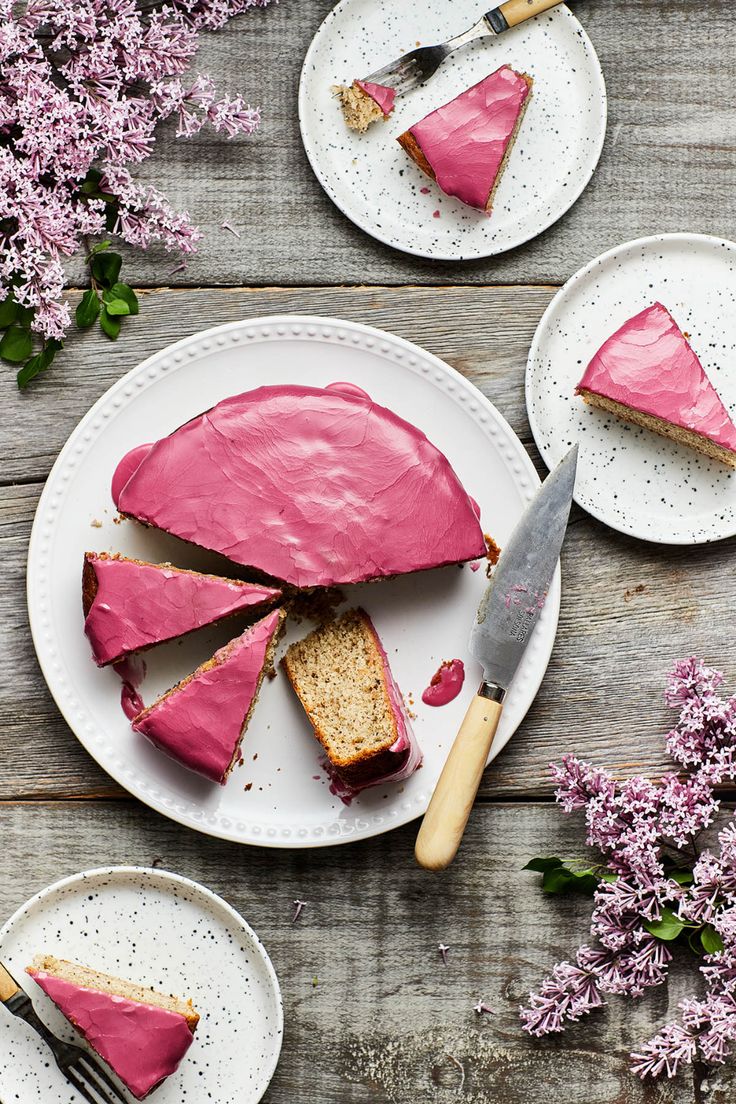 a piece of cake on a plate with pink frosting next to it and flowers