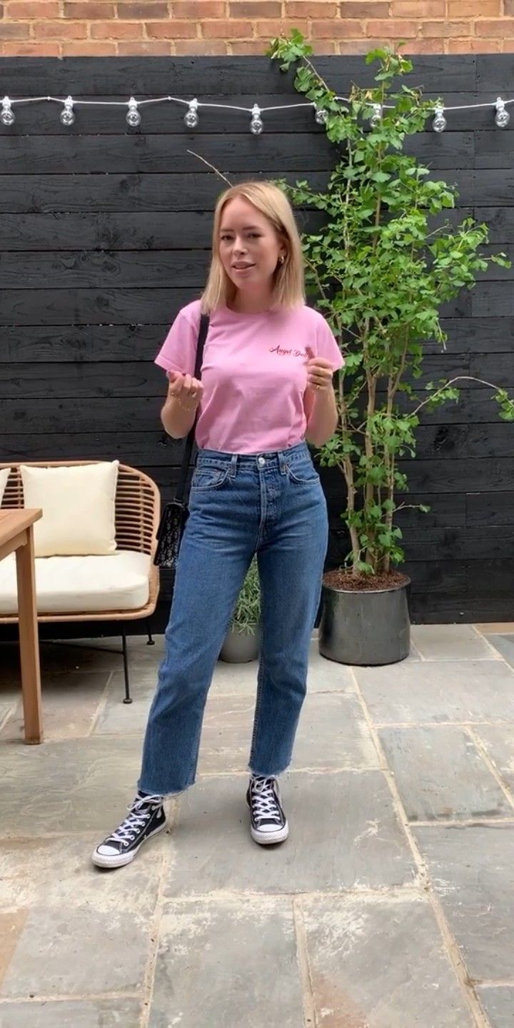 a woman in pink shirt and jeans standing on patio with potted plant behind her