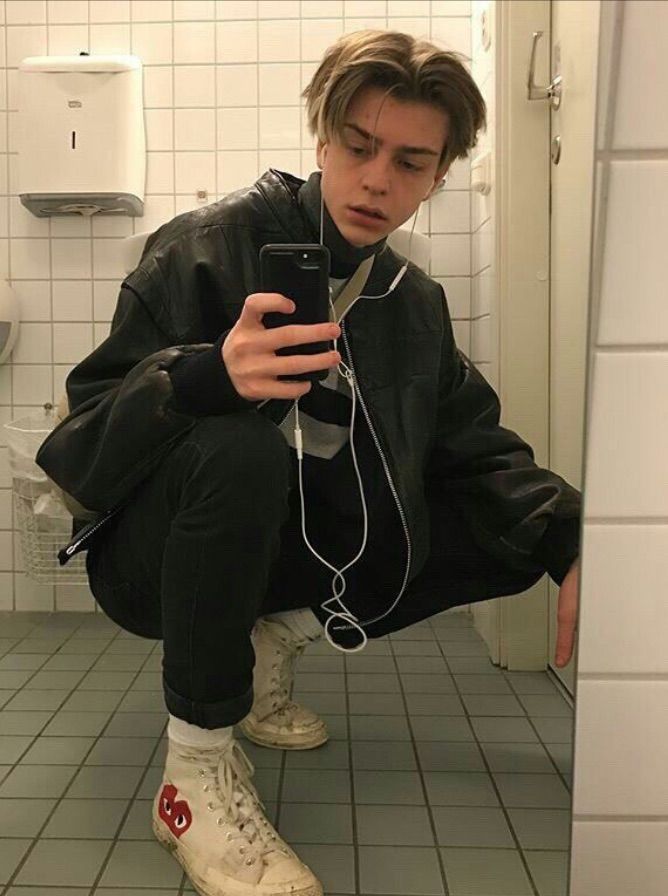 a young man squatting on the floor with headphones in his ears while looking at his cell phone