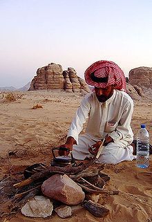 a man sitting on top of a sandy beach next to a pile of rocks and a bottle