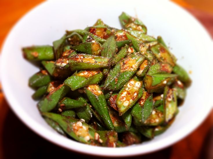 a white bowl filled with green beans on top of a wooden table and topped with seasoning