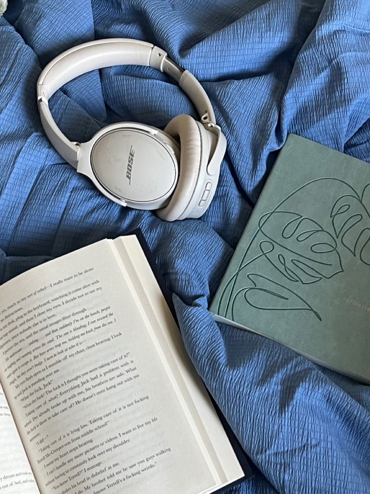 an open book and headphones on top of a blue bed with a pair of white headphones