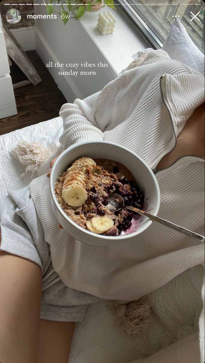 a woman is holding a bowl of oatmeal with bananas and blueberries