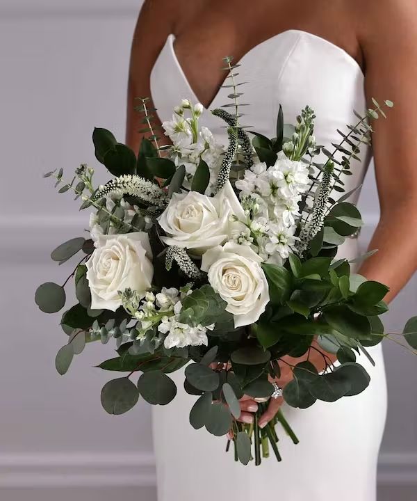 a bride holding a bouquet of white roses and greenery