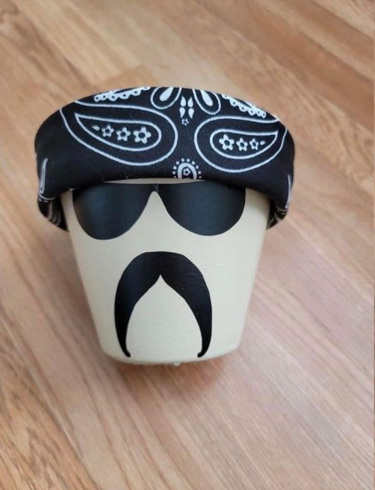 a black and white cup with a mustache on it's side sitting on a wooden floor