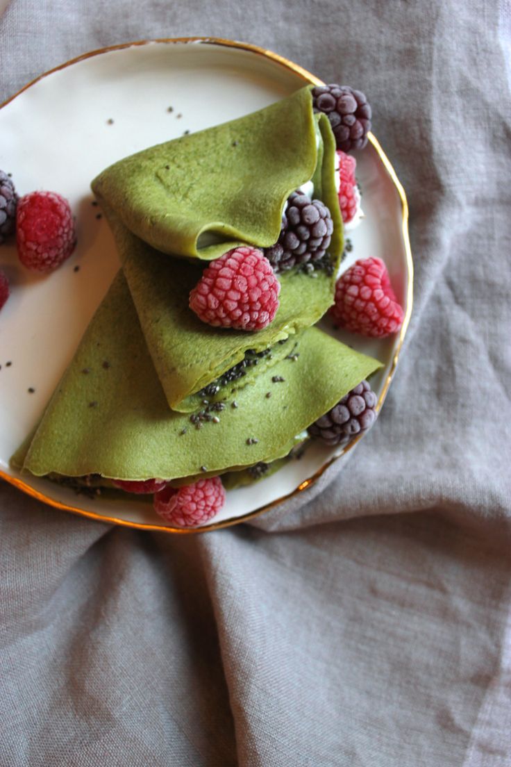 a plate topped with green pancakes covered in raspberries and blackberries on top of it