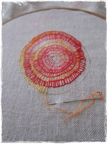 a close up of a piece of embroidery on a white cloth with an orange thread