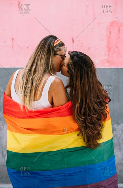 two beautiful young women hugging each other while wrapped in a rainbow colored blanket