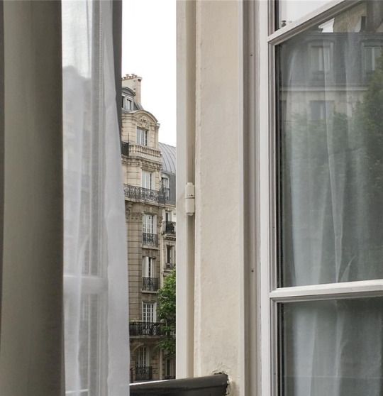 a cat sitting on top of a window sill next to an open window with curtains