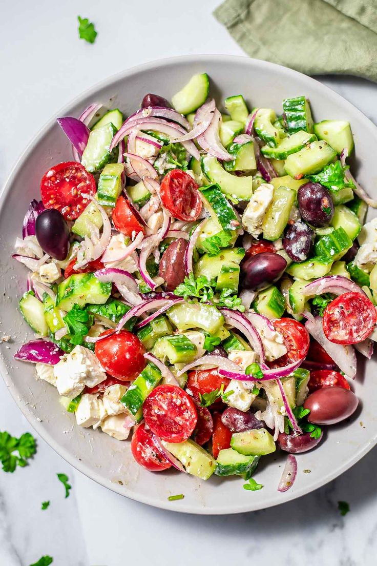 a salad with cucumbers, tomatoes, onions and olives in a white bowl