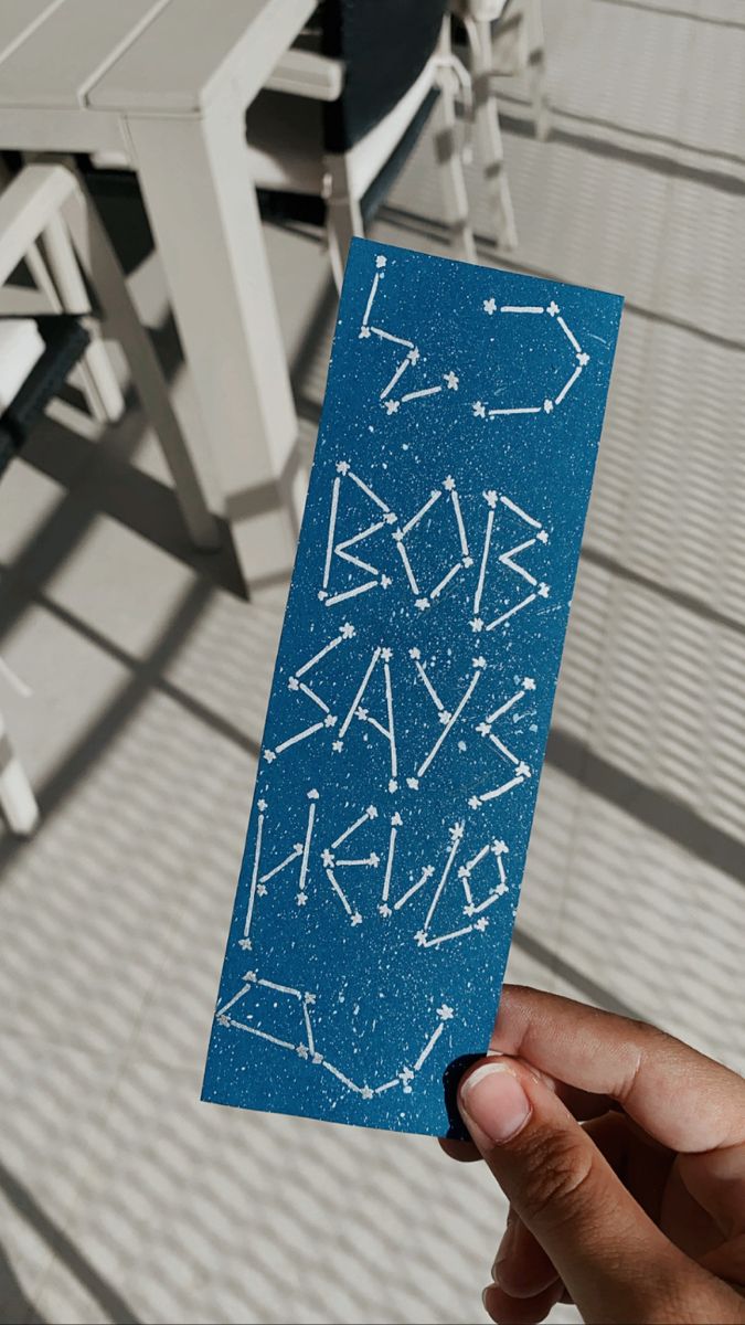 a hand holding up a blue card with white writing on it and stars in the sky