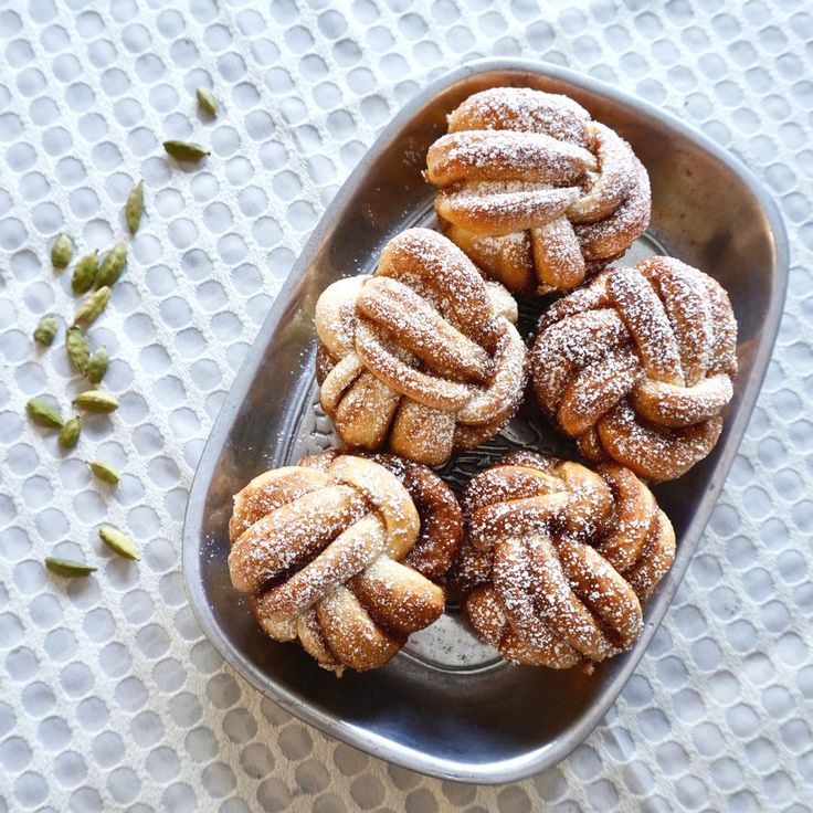 powdered sugar covered pastries in a metal dish on a white tablecloth with seeds