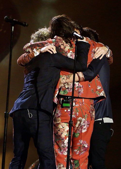 two women hugging each other while standing in front of a microphone and another woman with her arms around her head