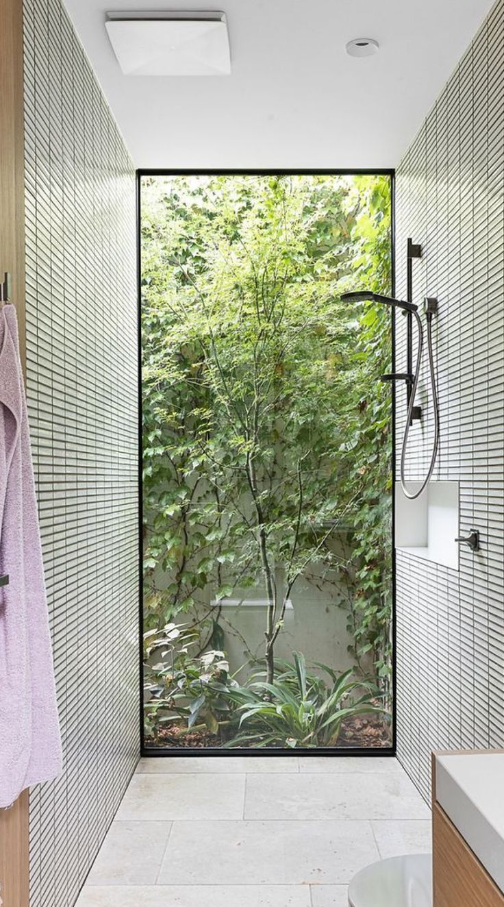 a bathroom with a glass door leading to the shower area and outside trees in the background