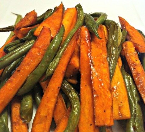 some green beans and carrots are on a white plate with brown sauce over them