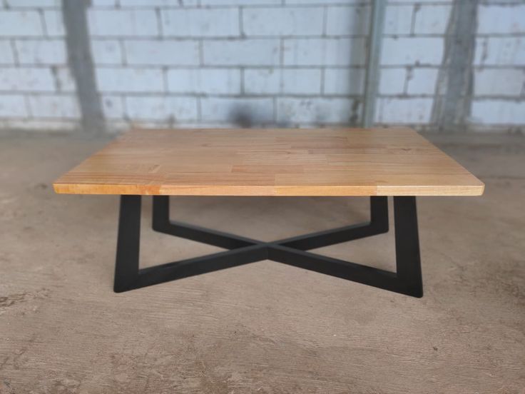 a wooden table sitting on top of a cement floor next to a brick wall with black metal legs