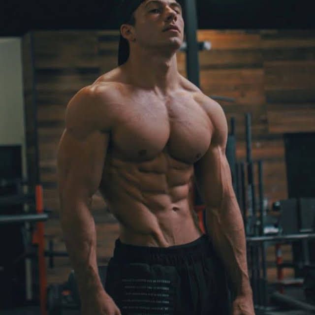 a shirtless man standing in a gym with his hands on his hips and looking up