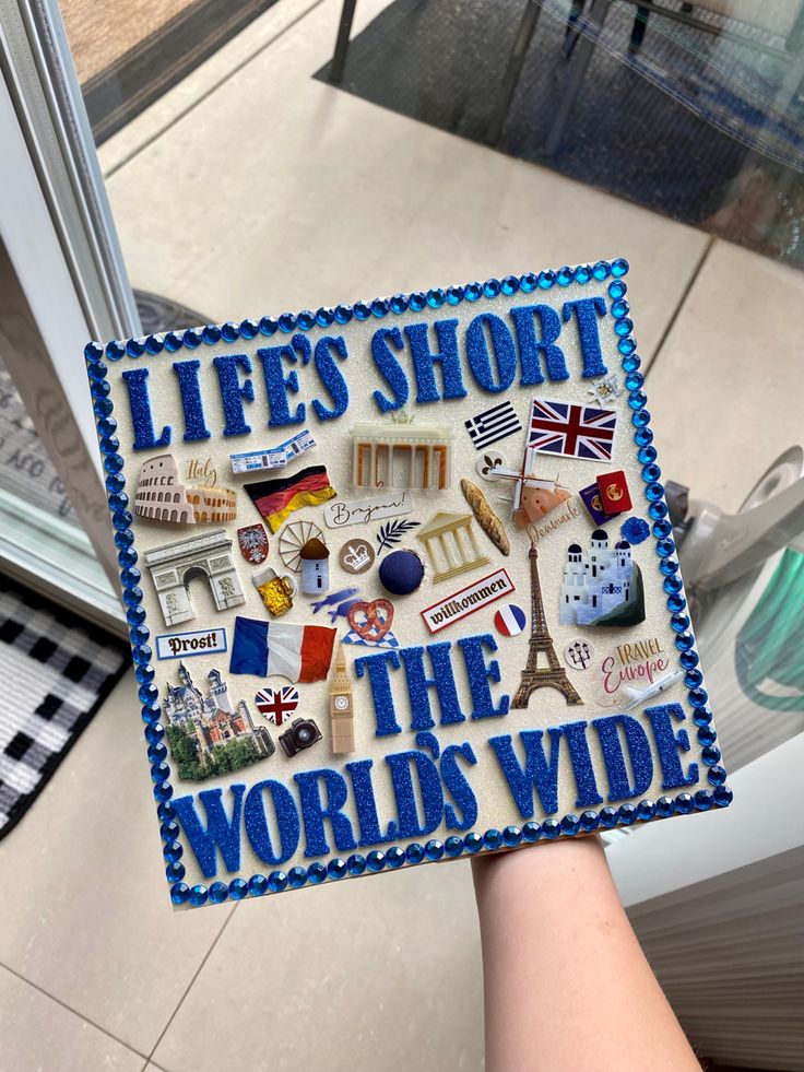 someone holding up a blue graduation cap that says life's short the world's wide