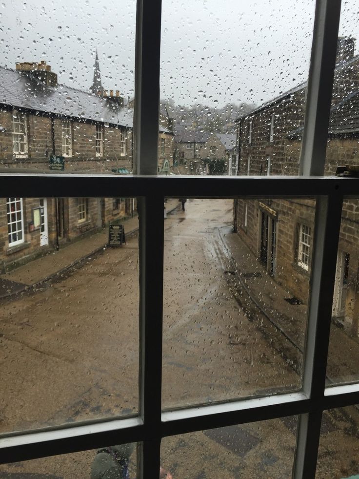 the rain is coming down on an empty street from inside a window looking out at some buildings