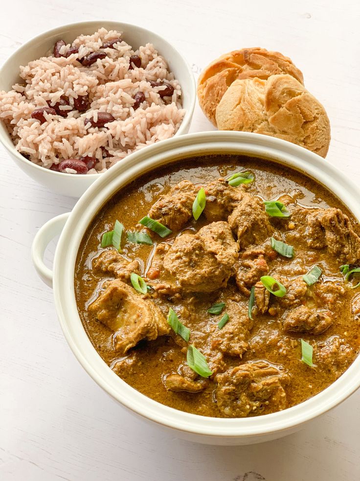 two bowls filled with meat and rice on top of a white table next to bread