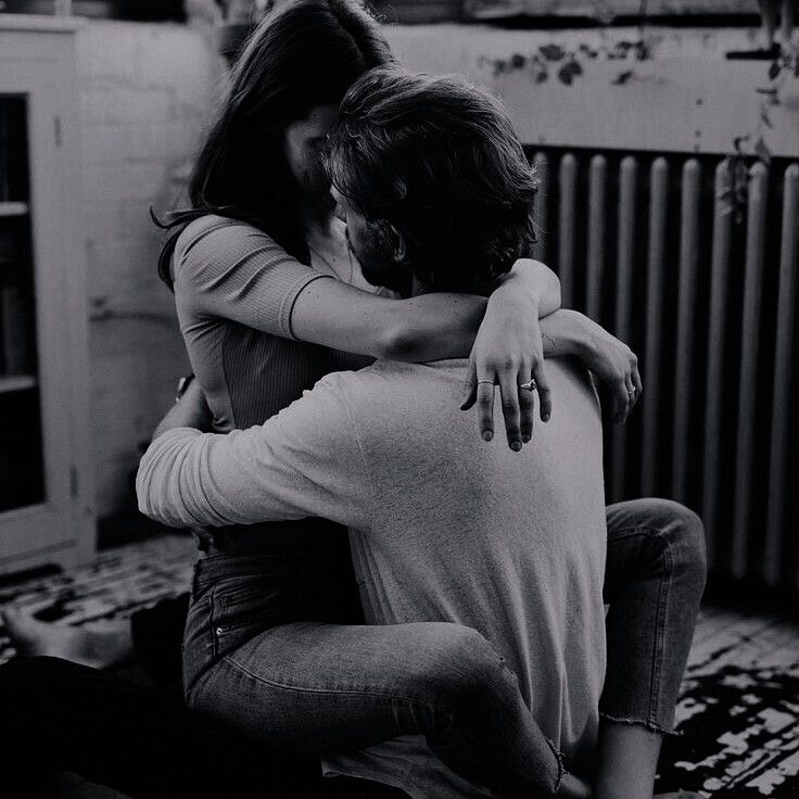 black and white photograph of two people hugging each other in front of a radiator