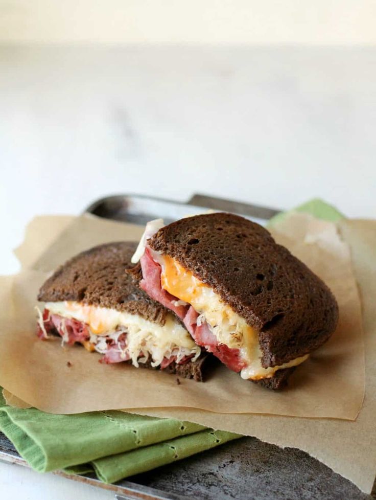 a sandwich with meat and cheese sitting on top of a piece of paper next to a fork