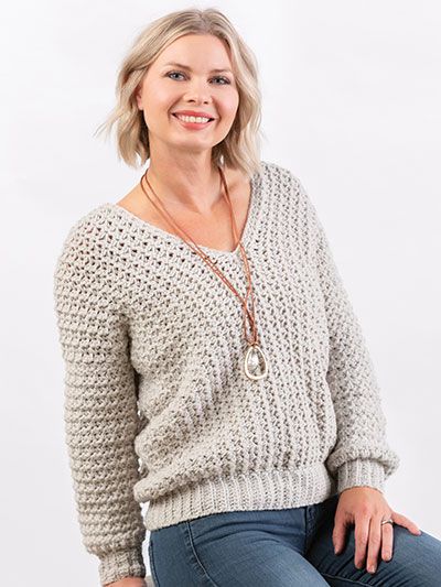 a woman sitting on top of a wooden stool wearing jeans and a sweater with an open v - neck