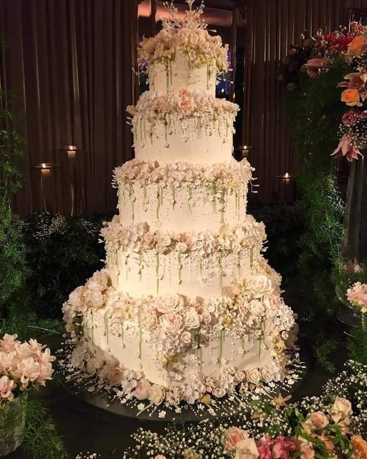 a large white wedding cake sitting on top of a table next to flowers and greenery