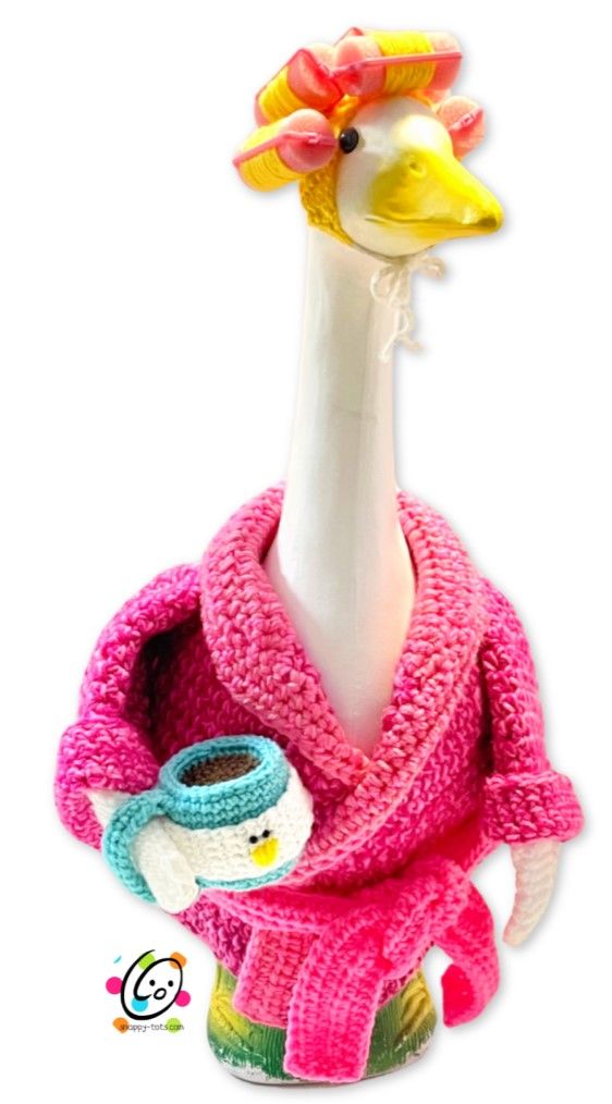 a knitted bird wearing a pink sweater with a cup in it's beak