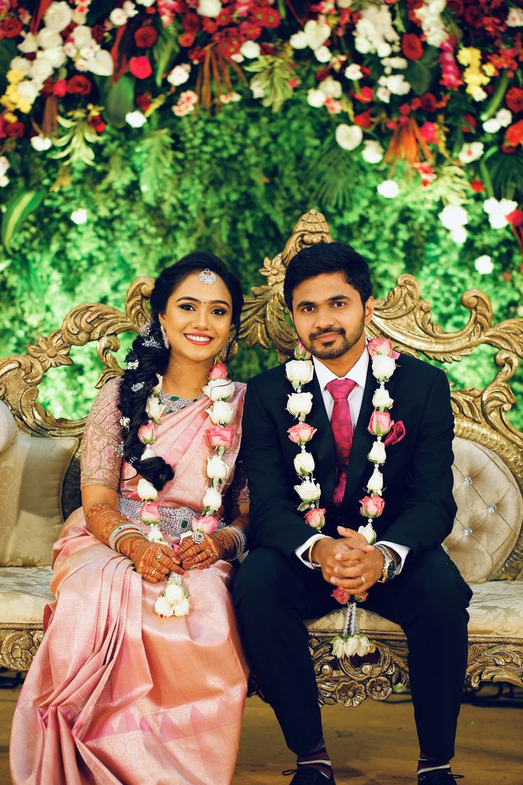 a man and woman sitting next to each other on a couch in front of flowers