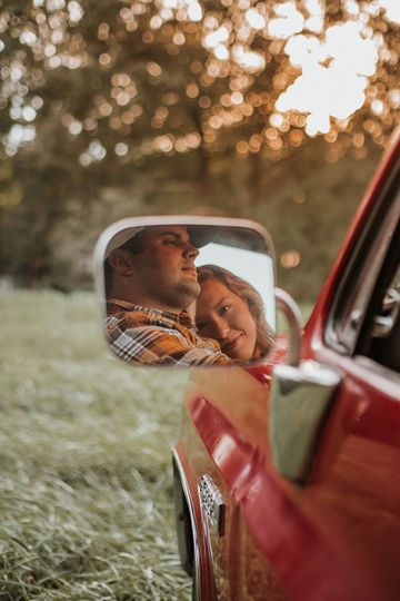 a man and woman are reflected in the side mirror of a red car on grass